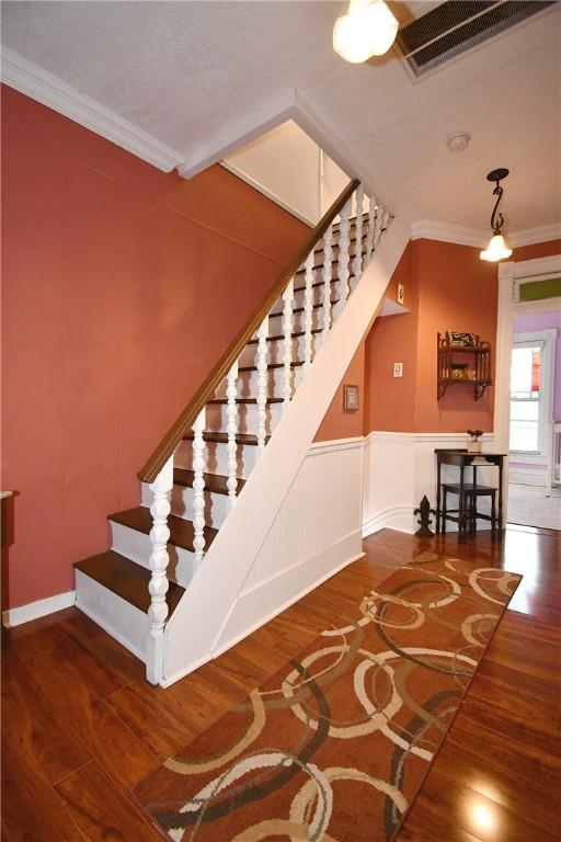 staircase featuring wood finished floors, ornamental molding, and wainscoting