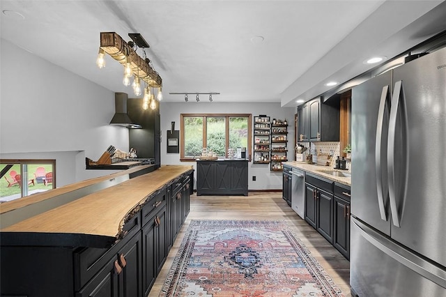 kitchen featuring appliances with stainless steel finishes, dark cabinets, light wood-type flooring, backsplash, and a sink
