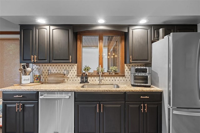 kitchen featuring stainless steel appliances, a sink, tasteful backsplash, and light stone countertops