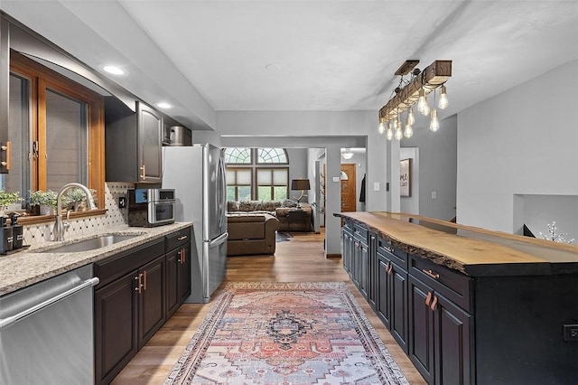 kitchen with stainless steel appliances, a sink, light wood finished floors, open floor plan, and decorative backsplash