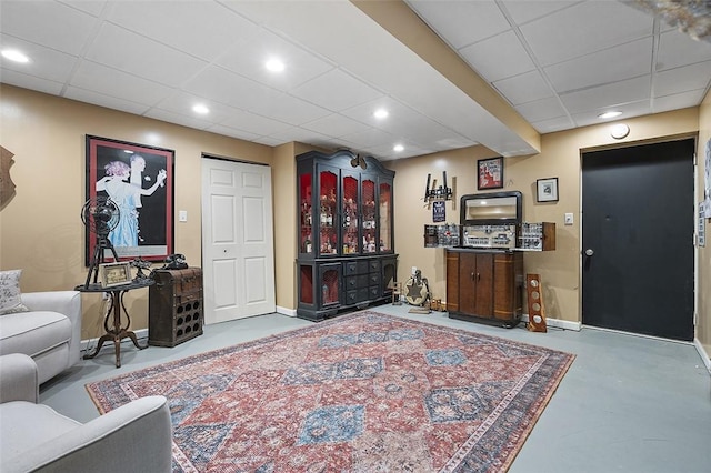 living area with a paneled ceiling, finished concrete flooring, recessed lighting, and baseboards