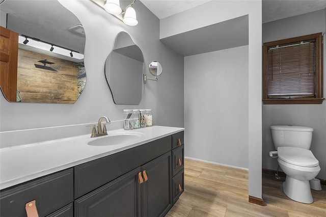 bathroom with wood finished floors, toilet, vanity, and baseboards