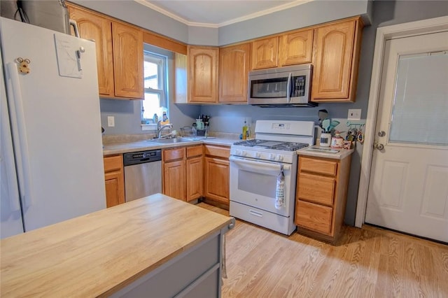 kitchen with appliances with stainless steel finishes, a sink, light wood finished floors, ornamental molding, and butcher block counters