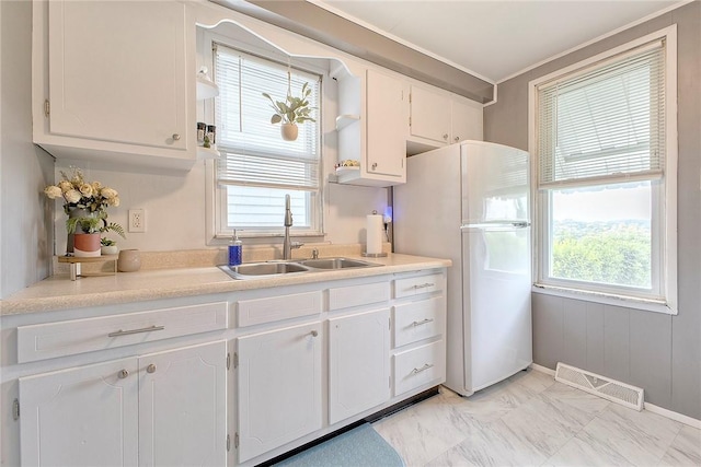 kitchen featuring a sink, white cabinets, freestanding refrigerator, and light countertops