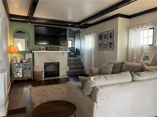 living room featuring wood finished floors, beam ceiling, and a brick fireplace