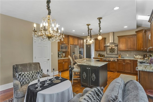 117 Majestic Dr, Adams Twp, PA 16046 - kitchen featuring wall chimney range hood, a chandelier, appliances with stainless steel finishes, brown cabinets, and a kitchen island