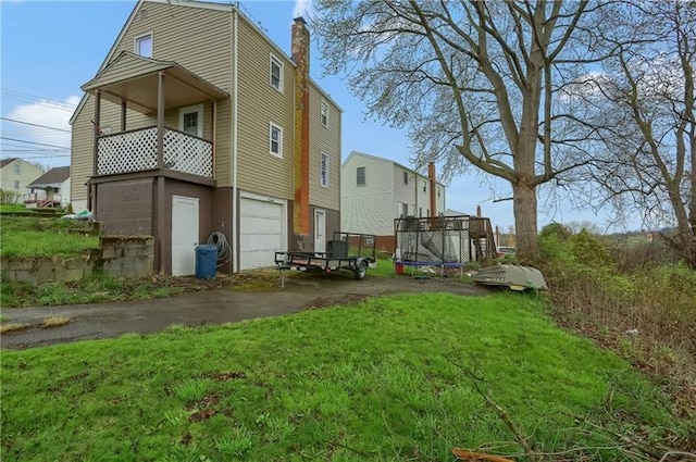 622 Ascension Dr, West Mifflin, PA 15122 - back of property with a trampoline, asphalt driveway, an attached garage, a chimney, and a yard