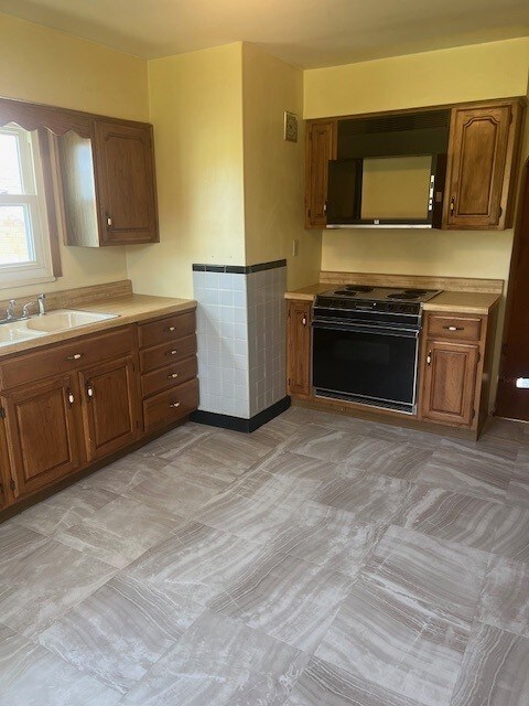 525 Glade Mill Run, Middlesex Twp, PA 16059 - kitchen featuring black / electric stove, a sink, brown cabinets, light countertops, and wainscoting