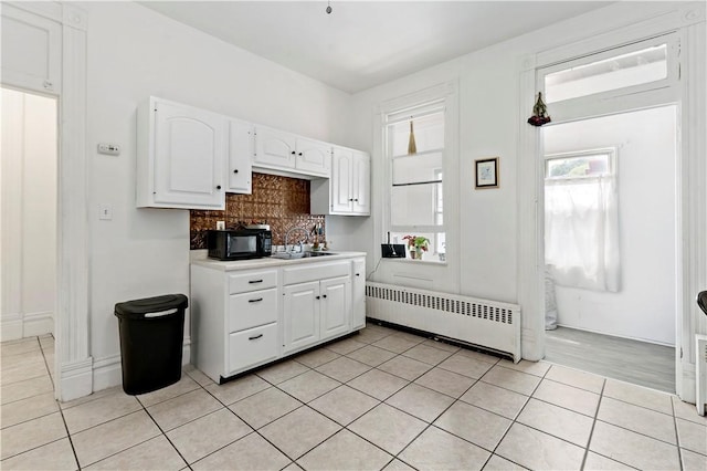 134 S 19th St, South Side, PA 15203 - kitchen featuring radiator, white cabinetry, light tile patterned floors, tasteful backsplash, and black microwave