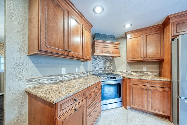 62 Spring St, Etna, PA 15223 - kitchen with appliances with stainless steel finishes, custom exhaust hood, backsplash, brown cabinetry, and a textured wall