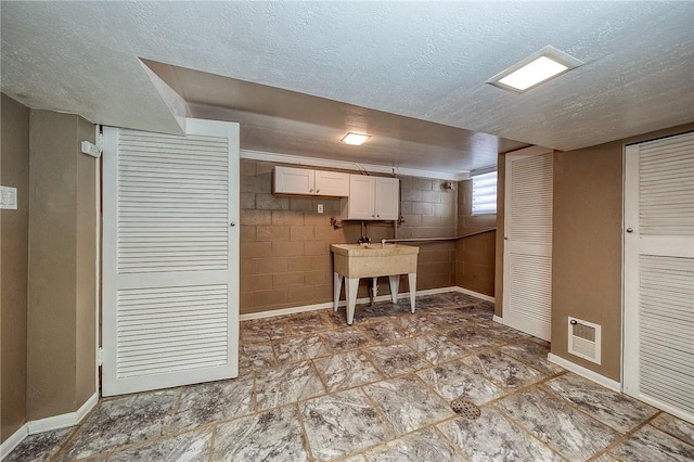 62 Spring St, Etna, PA 15223 - kitchen featuring a textured ceiling, baseboards, concrete block wall, and white cabinetry