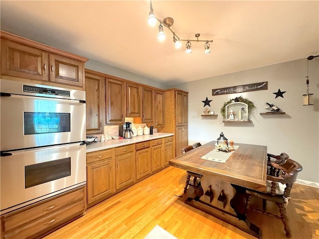 823 Irwin Dr, Baldwin Boro, PA 15236 - kitchen with stainless steel double oven, brown cabinetry, light countertops, light wood finished floors, and tasteful backsplash