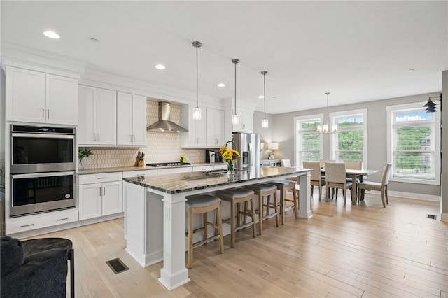 349 Azalea Dr, Peters Twp, PA 15367 - kitchen featuring wall chimney exhaust hood, appliances with stainless steel finishes, an island with sink, white cabinetry, and a kitchen breakfast bar