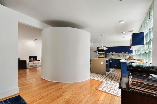 2219 Beechwood Blvd, Squirrel Hill, PA 15217 - kitchen with blue cabinets, light wood-style floors, a fireplace, tasteful backsplash, and a kitchen island
