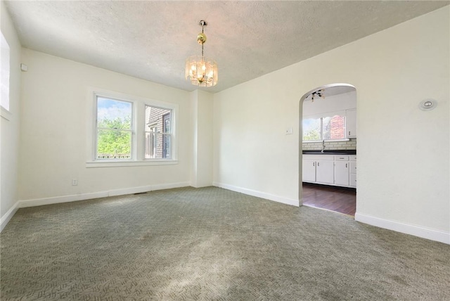 163 Universal Rd, Penn Hills, PA 15235 - spare room featuring dark colored carpet, a chandelier, arched walkways, a textured ceiling, and baseboards