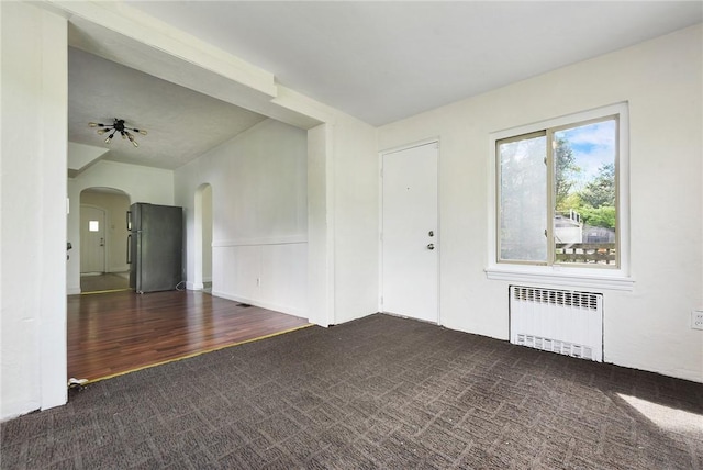 163 Universal Rd, Penn Hills, PA 15235 - unfurnished living room featuring radiator heating unit, arched walkways, carpet, and wood finished floors