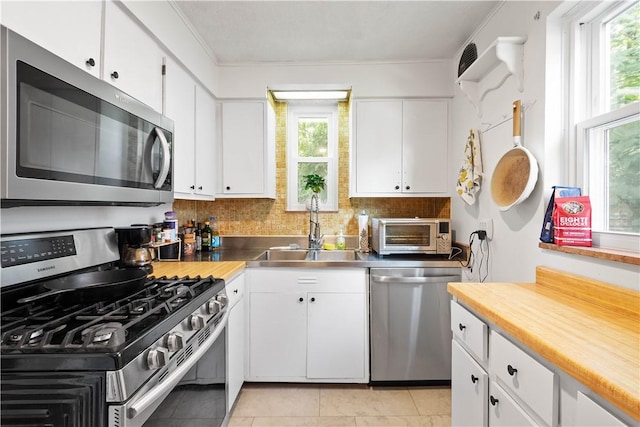 1415 Oakglen St, Crafton Heights, PA 15204 - kitchen featuring stainless steel appliances, stainless steel countertops, a sink, white cabinetry, and decorative backsplash
