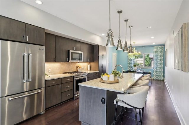 4707 Hatfield St, Lawrenceville, PA 15201 - kitchen featuring appliances with stainless steel finishes, dark brown cabinetry, dark wood finished floors, a kitchen island with sink, and a kitchen bar