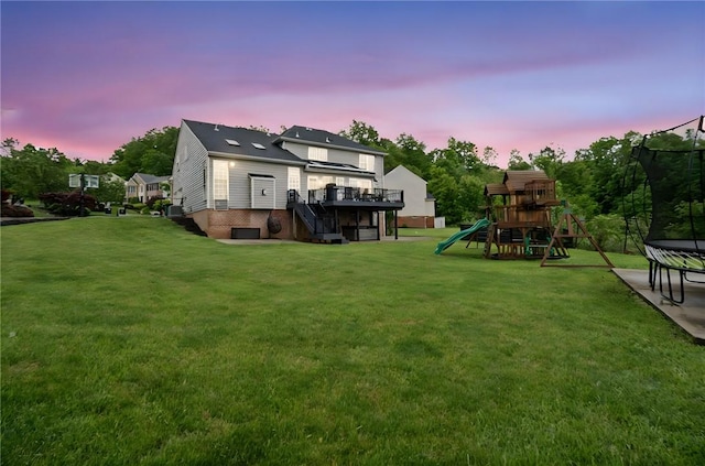 8426 David Dr, South Fayette, PA 15017 - back of house at dusk featuring a trampoline, a yard, stairs, a playground, and a wooden deck
