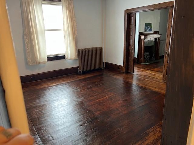 201 Thompson St, Latrobe, PA 15650 - unfurnished room with radiator heating unit, wood-type flooring, a fireplace, and baseboards