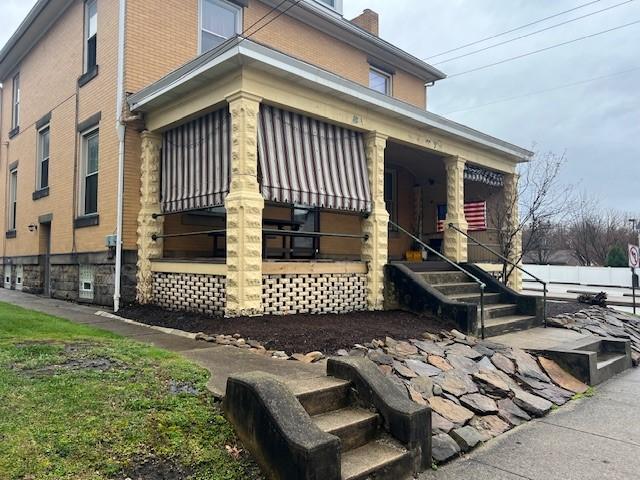 201 Thompson St, Latrobe, PA 15650 - view of side of property featuring covered porch, brick siding, a chimney, and stairs