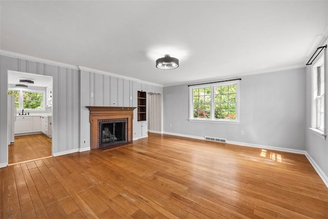 1509 Walnut St, Edgewood, PA 15218 - unfurnished living room with crown molding, a fireplace, light wood-style flooring, and plenty of natural light