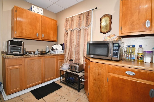 108 Locust St, Mount Oliver, PA 15210 - kitchen with stainless steel microwave, light tile patterned floors, brown cabinetry, a drop ceiling, and light countertops