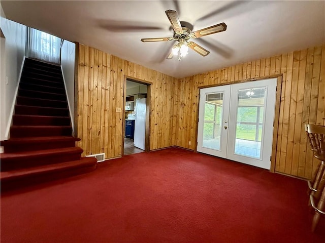 2225 Pleasantview Dr, Manor Twp, PA 16226 - unfurnished living room featuring french doors, wood walls, stairs, dark colored carpet, and a ceiling fan