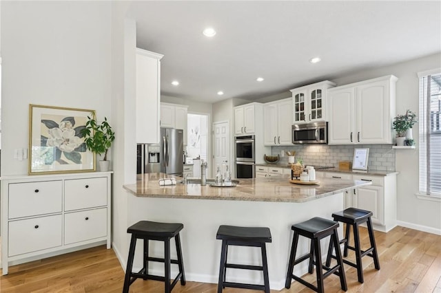 319 Buffalo Ridge Rd, Peters Twp, PA 15317 - kitchen featuring appliances with stainless steel finishes, a breakfast bar area, decorative backsplash, white cabinetry, and light wood-type flooring
