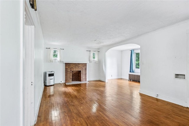 624 Frayne St, Greenfield, PA 15207 - unfurnished living room featuring arched walkways, radiator, hardwood / wood-style flooring, a textured ceiling, and a brick fireplace