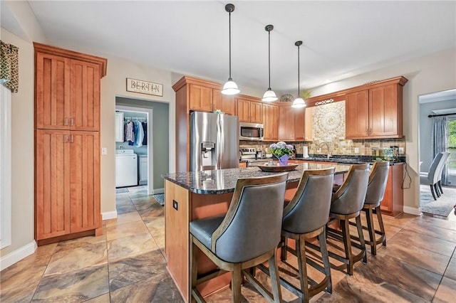 2104 Pierce Bluffs Dr, Hermitage, PA 16148 - kitchen featuring stainless steel appliances, washer / dryer, decorative backsplash, a kitchen island, and a breakfast bar
