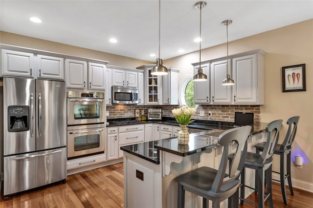 104 Southridge Dr, Cranberry Twp, PA 16066 - kitchen featuring appliances with stainless steel finishes, a peninsula, tasteful backsplash, wood finished floors, and glass insert cabinets