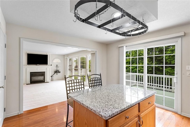 117 Trailside Ct, North Fayette, PA 15108 - kitchen featuring light wood-type flooring, a fireplace with flush hearth, light stone counters, a kitchen breakfast bar, and a kitchen island