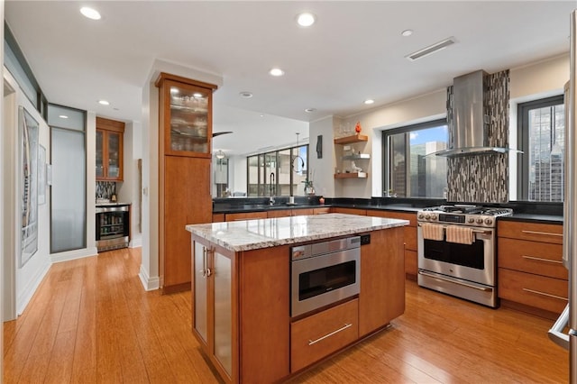 151 Fort Pitt Blvd Unit 1703, Downtown Pgh, PA 15222 - kitchen with stainless steel range with gas stovetop, wall chimney range hood, brown cabinetry, beverage cooler, and recessed lighting