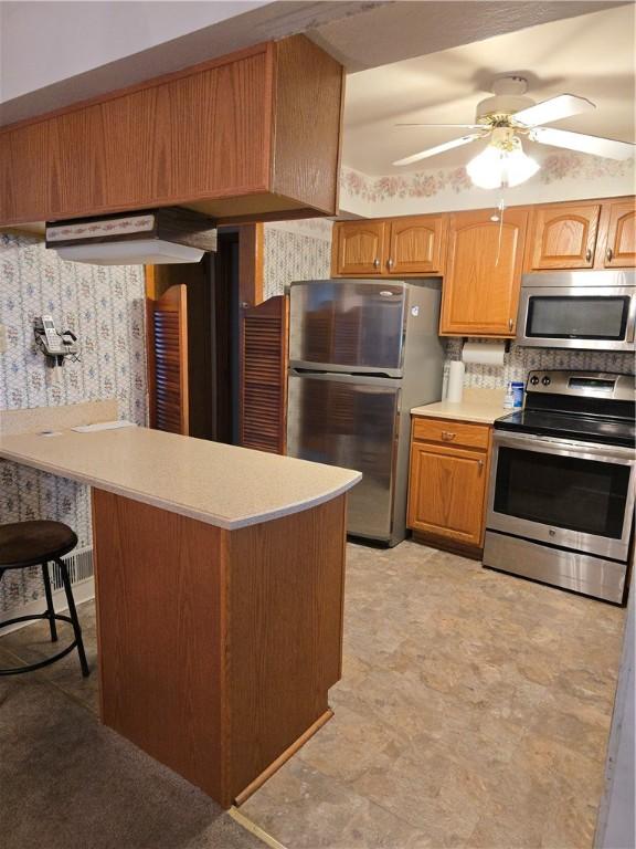 209 Pawnee St, Rostraver, PA 15012 - kitchen with stainless steel appliances, light countertops, wallpapered walls, ceiling fan, and a peninsula