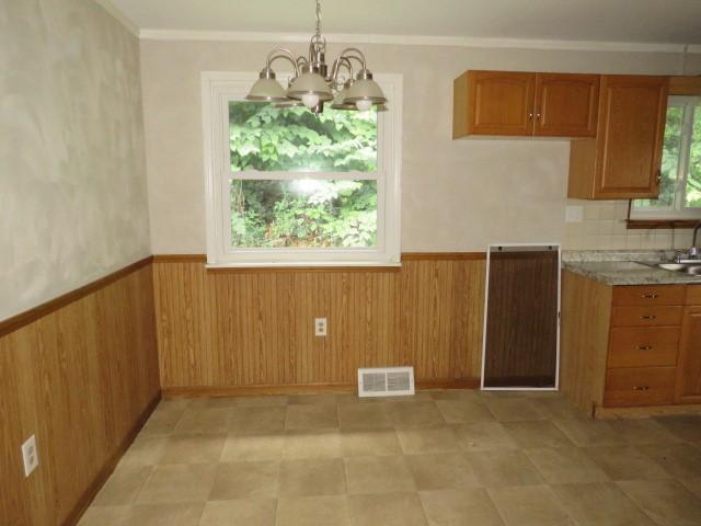 21 Daisytown Rd, W Pike Run Twp, PA 15427 - kitchen with a chandelier, brown cabinetry, wainscoting, wooden walls, and hanging light fixtures