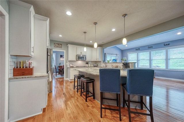 1517 Lombard Cir, South Strabane, PA 15301 - kitchen featuring appliances with stainless steel finishes, white cabinetry, a kitchen breakfast bar, backsplash, and light wood-type flooring