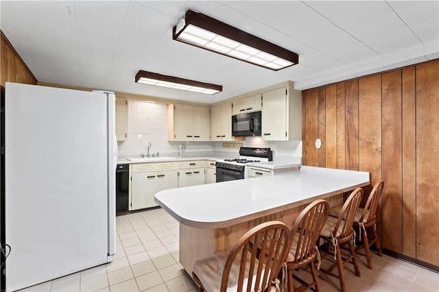 146 Samuel St, Chippewa Twp, PA 15010 - kitchen with black appliances, a sink, a peninsula, light tile patterned flooring, and wood walls