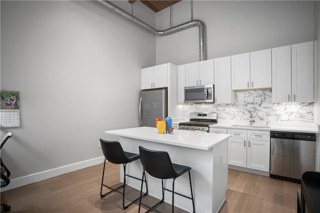 622 Gross St Unit 104, Bloomfield, PA 15224 - kitchen featuring appliances with stainless steel finishes, a sink, a breakfast bar area, backsplash, and a towering ceiling