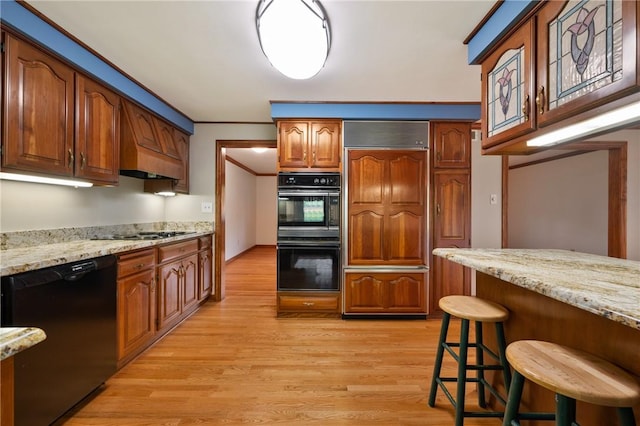 2525 Chapelwood Dr, Upper St Clair, PA 15241 - kitchen featuring black appliances, light wood-type flooring, a kitchen breakfast bar, light stone countertops, and brown cabinets