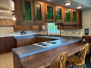 1877 Main St, Arona, PA 15617 - kitchen featuring a peninsula, ceiling fan, a kitchen breakfast bar, white cooktop, and glass insert cabinets