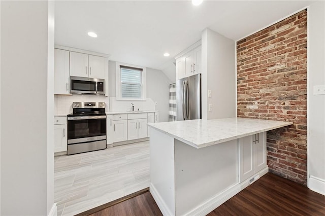 1110 Illinois Ave, Dormont, PA 15216 - kitchen with appliances with stainless steel finishes, light wood finished floors, white cabinetry, light stone countertops, and brick wall