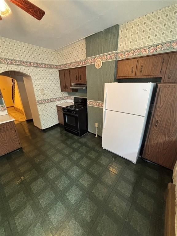 7027 Blackhawk St, Swissvale, PA 15218 - kitchen with freestanding refrigerator, black stove, wallpapered walls, extractor fan, and arched walkways