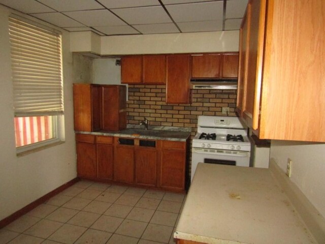 1214 1/2 3rd St, Mckees Rocks, PA 15136 - kitchen with white range with gas stovetop, a drop ceiling, brown cabinets, baseboards, and under cabinet range hood