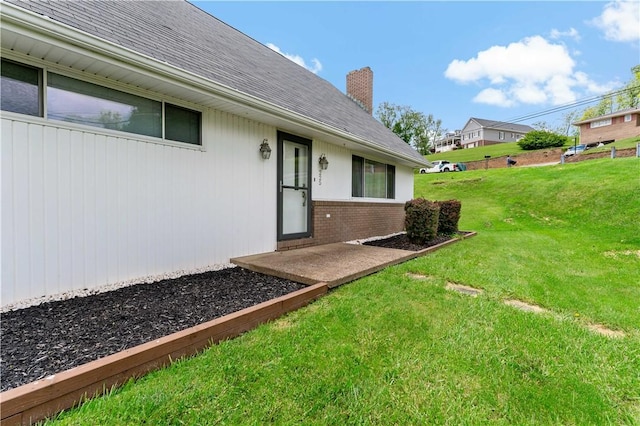 225 Larson Blvd, Rostraver, PA 15012 - view of exterior entry with brick siding, a chimney, a yard, and roof with shingles