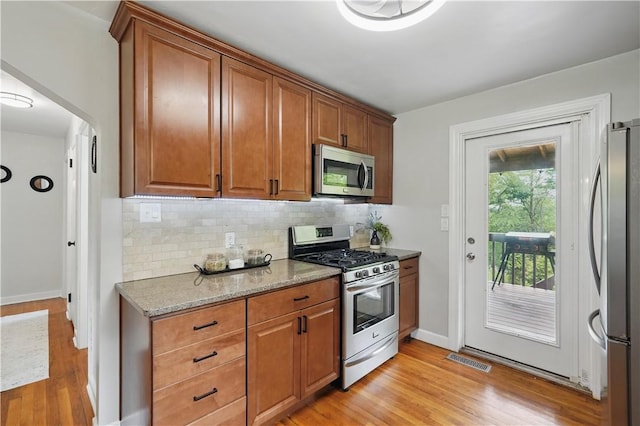9440 Peebles Rd, Mccandless, PA 15101 - kitchen with appliances with stainless steel finishes, light wood finished floors, decorative backsplash, brown cabinetry, and light stone counters
