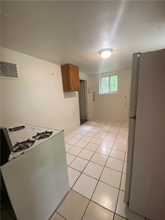 7740 Pershing St, Penn Hills, PA 15235 - kitchen featuring freestanding refrigerator, light tile patterned floors, and brown cabinetry