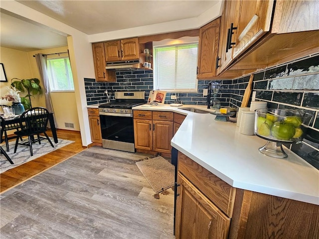 116 Bellwood Rd, West Mifflin, PA 15122 - kitchen featuring gas range, a sink, under cabinet range hood, brown cabinetry, and decorative backsplash