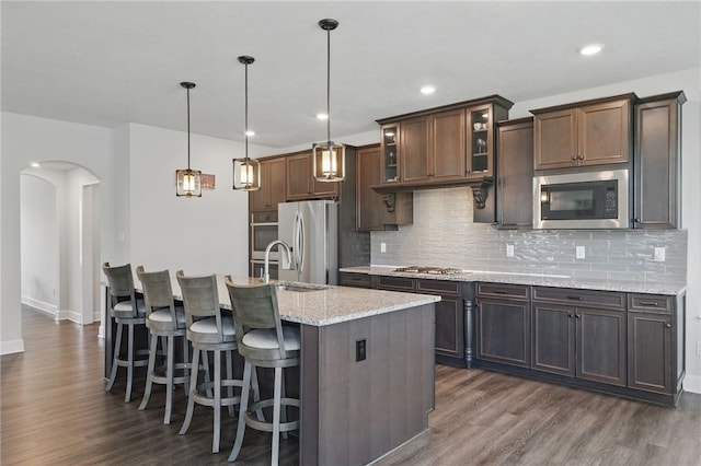 5023 Kensington Dr, Cecil, PA 15317 - kitchen featuring appliances with stainless steel finishes, dark wood finished floors, arched walkways, decorative backsplash, and a center island with sink