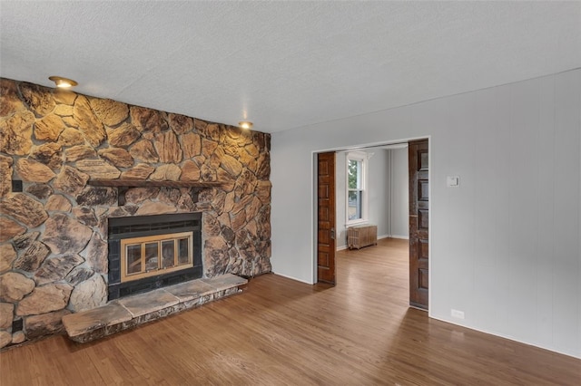 901 Punta Gorda Ave, East Mckeesport, PA 15035 - unfurnished living room with radiator heating unit, wood finished floors, a fireplace, a textured ceiling, and baseboards